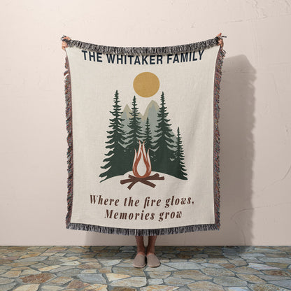 Blanket with 'The Whitaker Family' text and nature design held by a person against a plain wall.