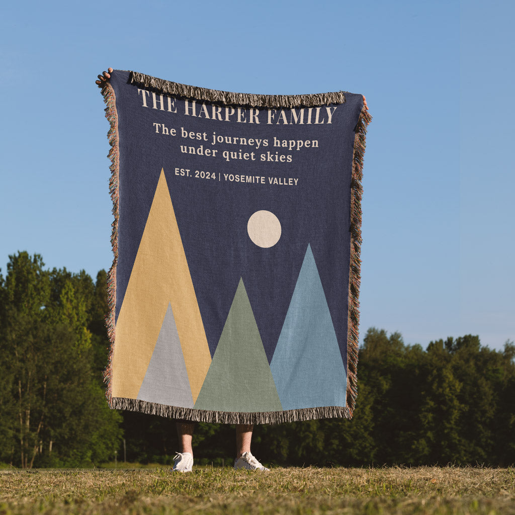 Blanket with mountain design and text held by a person in a field